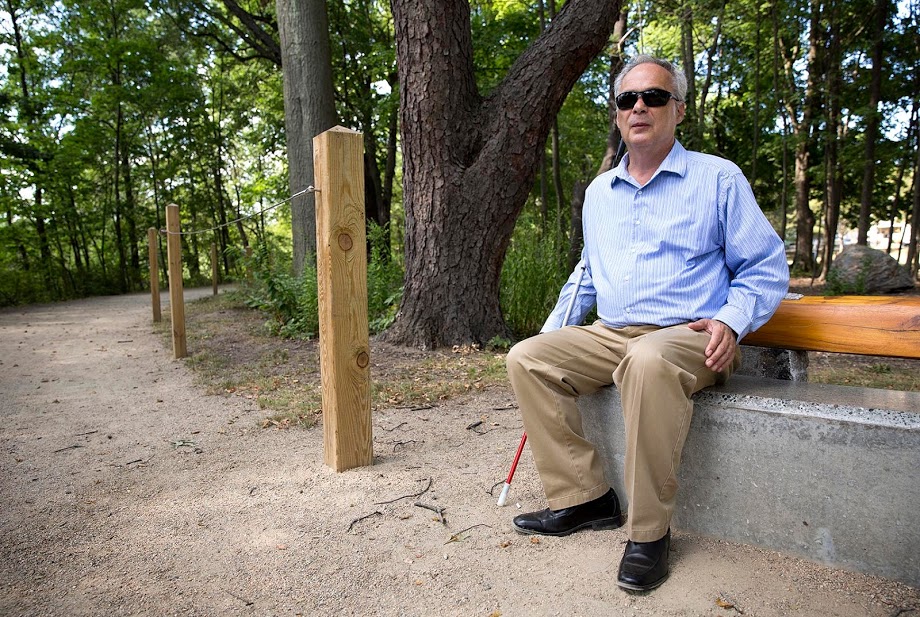Jerry Berrier sits in the Watertown Riverfront Park and Braille Trail, which was created by design firm Sasaki. (Robin Lubbock/WBUR)