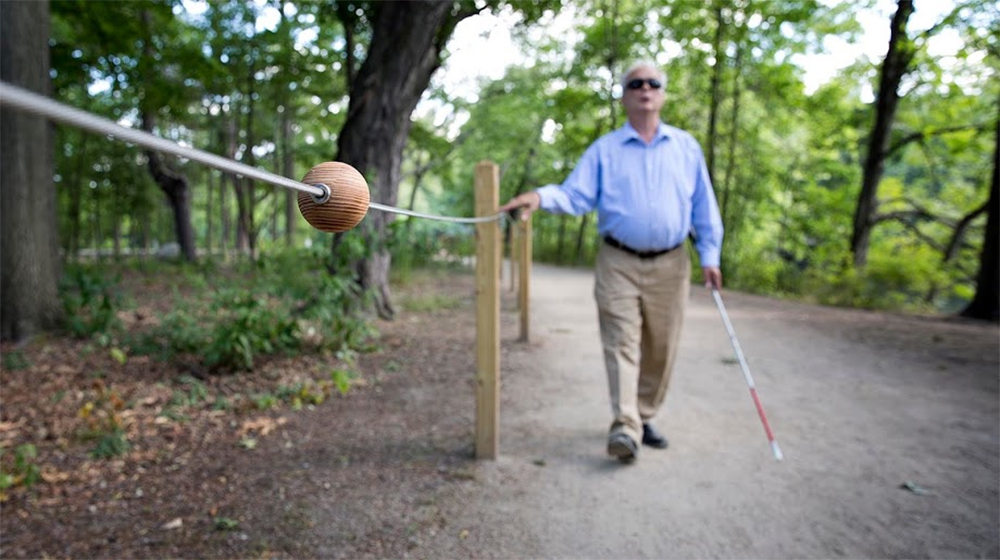Following a cable along the braille trail in Watertown, Jerry Berrier, 64, approaches a spherical block, which will tell him that there's a bench on the opposite side of the trail. (Robin Lubbock/WBUR)