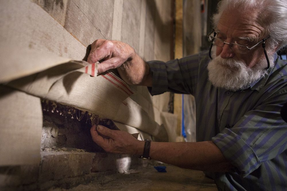 Professor Emeritus of Art Conservation at Queens University Ian Hodkinson reveals the original metal support system that helps hold the Pierre Puvis de Chavannes &quot;Philosophy&quot; mural in place. The mural is one of a 7-panel mural on display in the Grand Staircase at the main branch of the Boston Public Library. (Jesse Costa/WBUR)