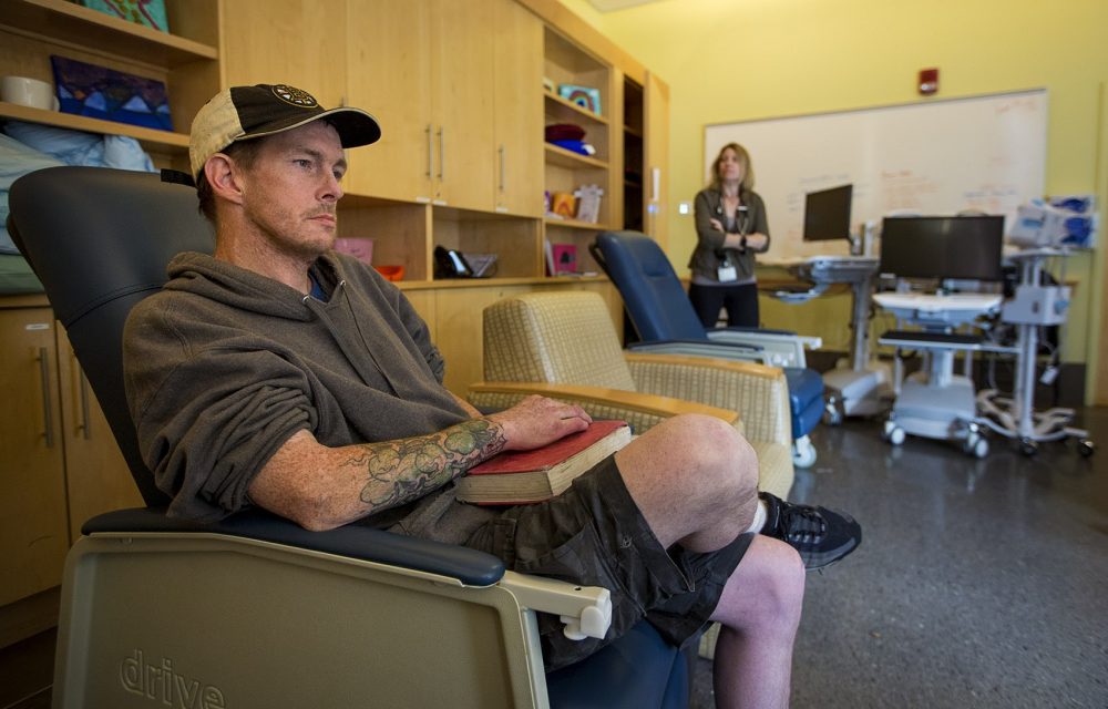 Tommy, a repeat SPOT patient, says the room has -- and will continue to -- save lives. Meanwhile Dr. Jessie Gaeta, chief medical officer at the Boston Health Care for the Homeless Program, watches him from the rear of the room. (Jesse Costa/WBUR) 