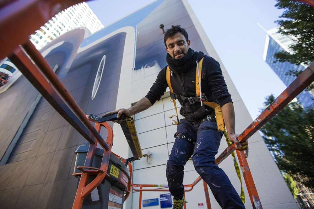 Iranian artist Mehdi Ghadyanloo climbs into a cherry picker as he works on the latest mural to go up on the Rose Kennedy Greenway in Dewey Square. (Jesse Costa/WBUR)