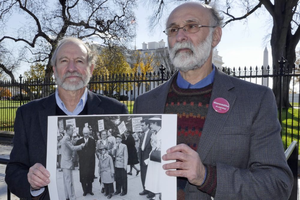 Michael (left) and Robert Meeropol demonstrating outside the White House on Dec. 1, 2016, holding a photograph of themselves demonstrating as children in 1953. (Courtesy Alan Heath/Rosenberg Fund for Children)