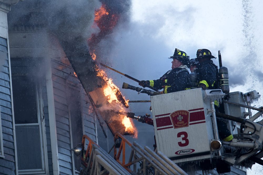 Boston firefighters pull down some siding to uncover flames to extinguish at a fire at 142-144 Bunker Hill St. in Charlestown. (Jesse Costa/WBUR)