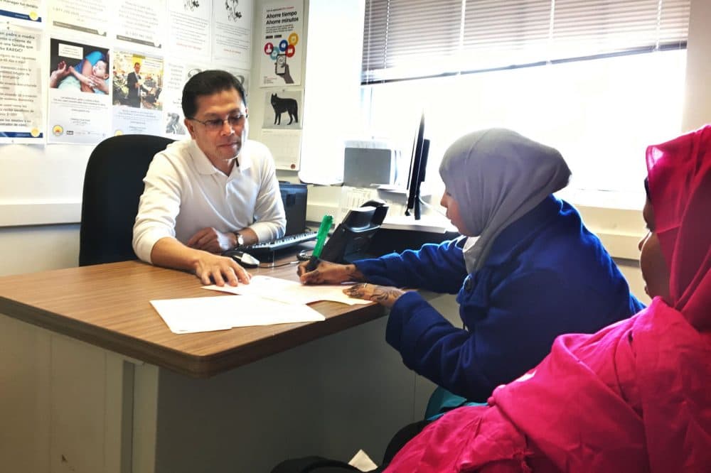 Hawo Ahmed (far right) signs her application for emergency food assistance (SNAP) at the DTA office in Lowell. (Shannon Dooling/WBUR)