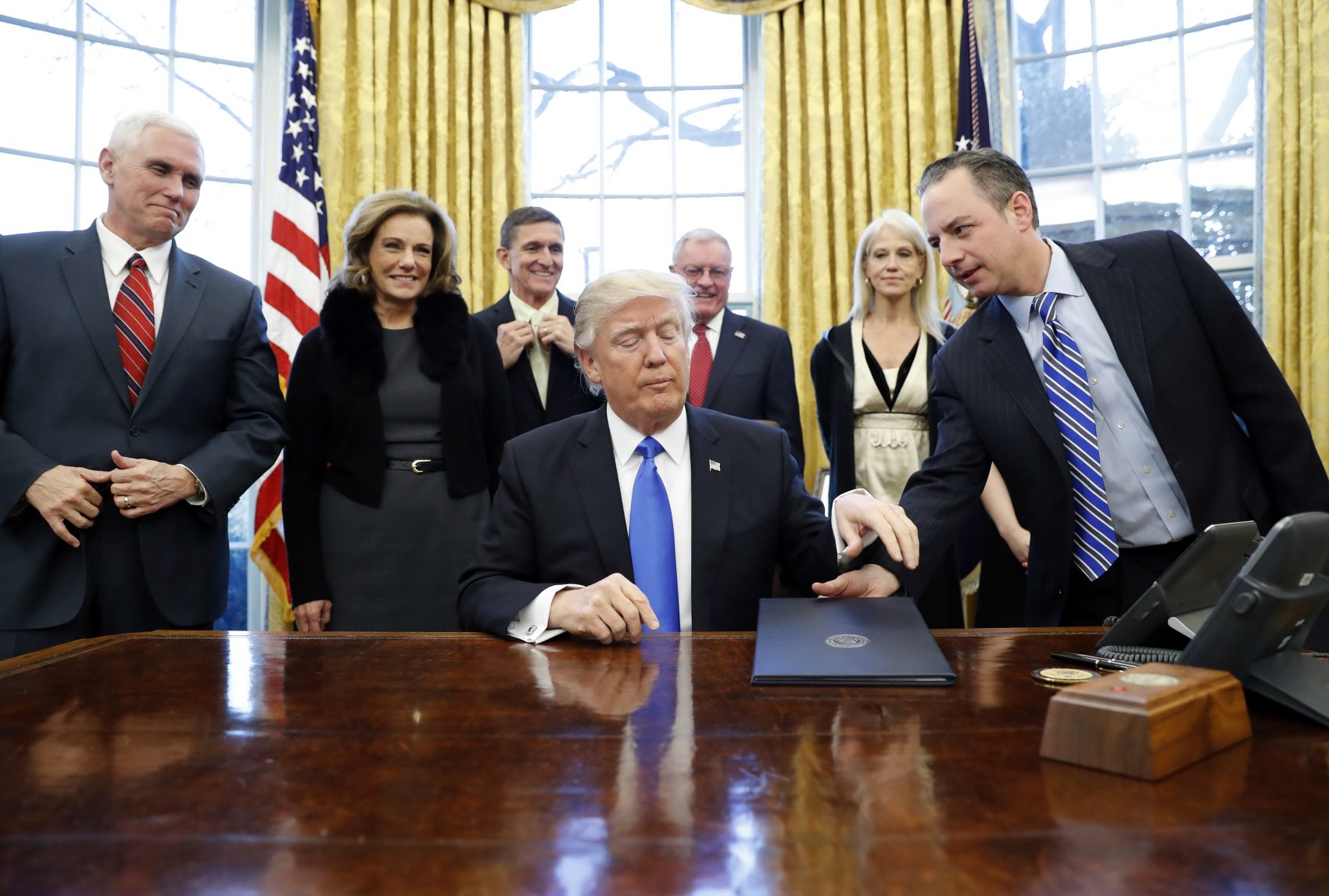 President Donald Trump is handed an Executive Order to sign by White House Chief of Staff Reince Priebus with Vice President Mike Pence and others in the Oval Office Saturday. (Alex Brandon/AP)