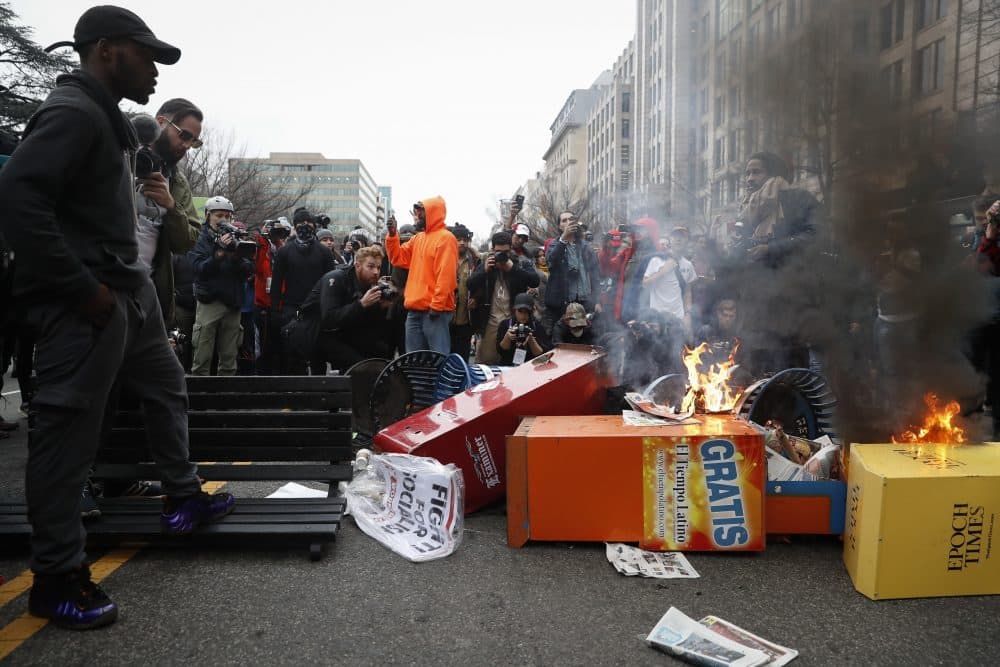 A Washington resident, left, guards a pile of burning newspaper machines to prevent protesters from feeding the flames while demanding peace in the streets during a demonstration after President Trump's inauguration. (John Minchillo/AP)