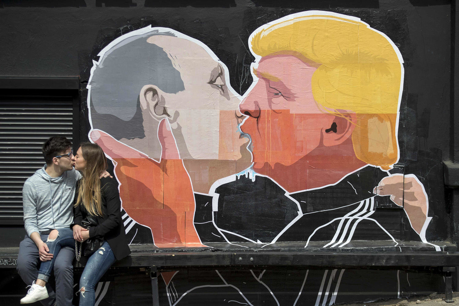 In this Saturday, May 14, 2016 file photo a couple kisses in front of graffiti depicting Russian President Vladimir Putin, left, and Republican presidential candidate Donald Trump, on the walls of a bar in the old town in Vilnius, Lithuania. (Mindaugas Kulbis/AP)