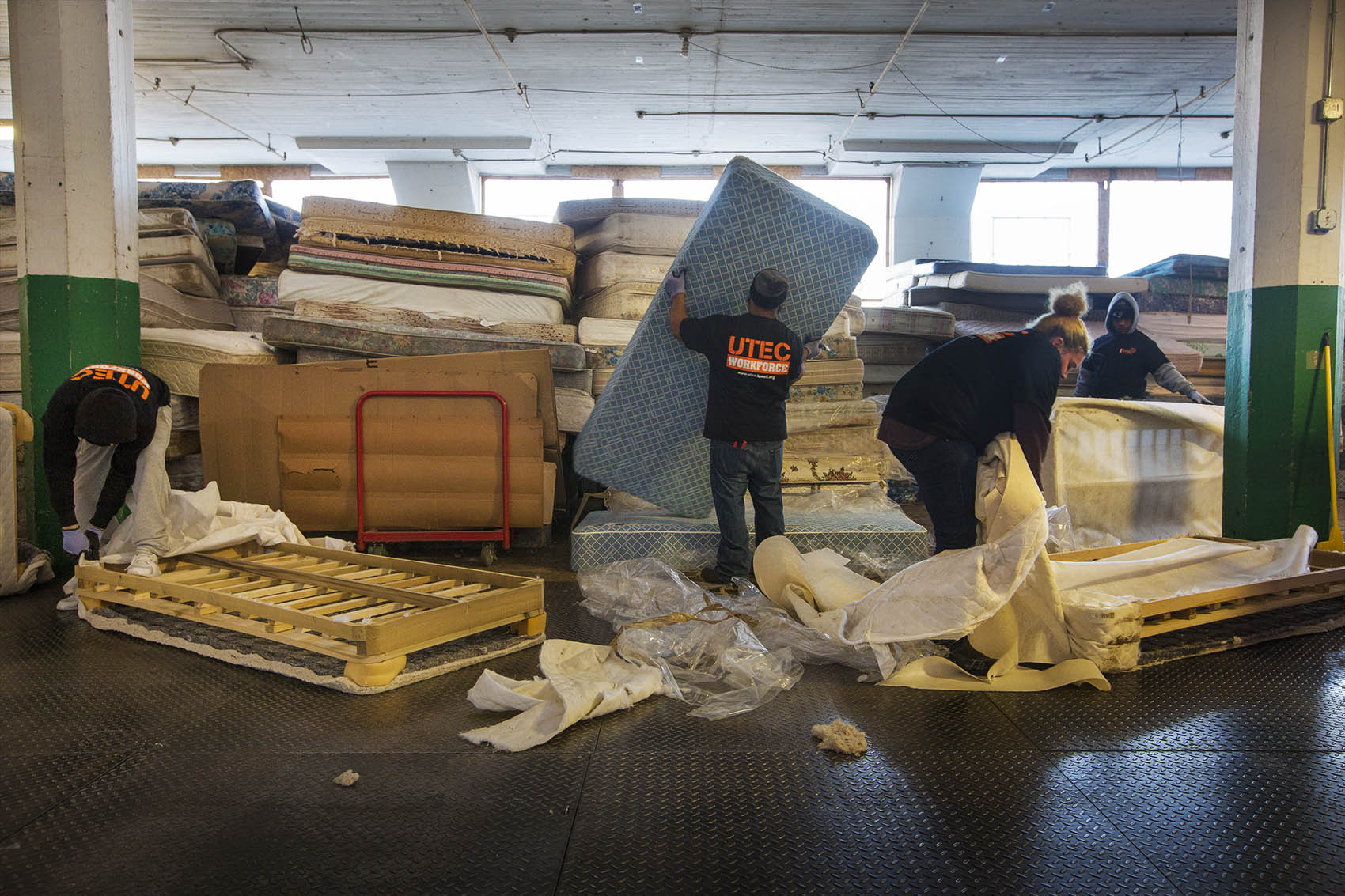 Workers at the UTEC mattress warehouse break down piles of mattresses. (Jesse Costa/WBUR)