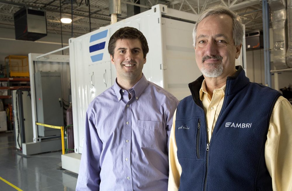 Ambri Chief Technology Officer Dave Bradwell and Chief Executive Officer Phil Giudice stand by a container holding a prototype battery unit. (Robin Lubbock/WBUR)