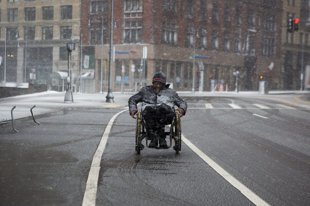 A man in a wheelchair battles the snow and wind passing City Hall Plaza in the bike lane on Cambridge Street. (Jesse Costa/WBUR)