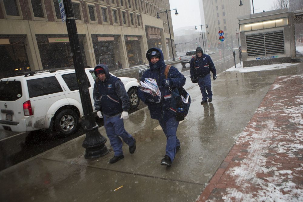 The blizzard isn't keeping the mail from being delivered today. Three mail carriers walk through City Hall Plaza. (Jesse Costa/WBUR)