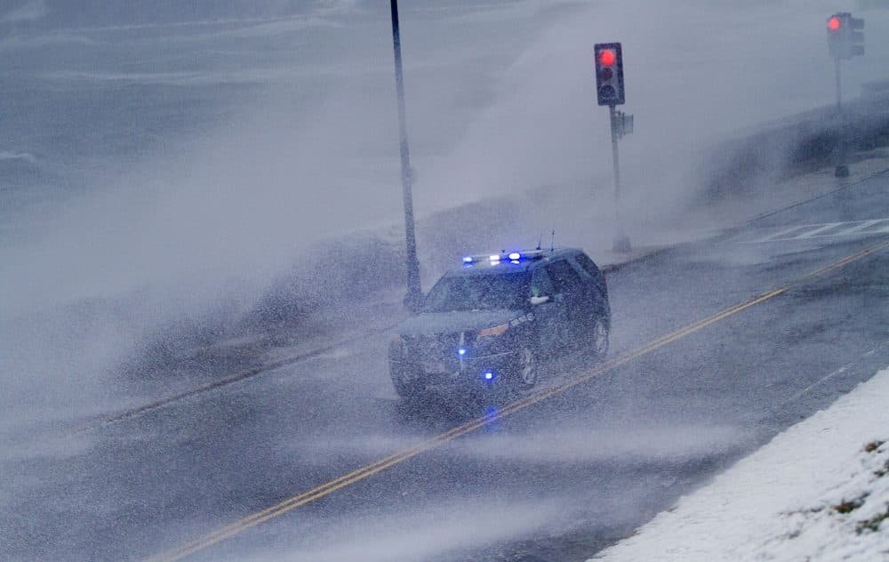 A Mass. State Police vehicle gets drives along Winthrop Parkway in Revere as waves crash over the seawall Tuesday afternoon. (Jesse Costa/WBUR)