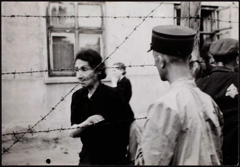 Henryk Ross photo of Lodz Ghetto police with woman behind barbed wire at the ghetto, 1942. (Courtesy, Museum of Fine Arts, Boston)