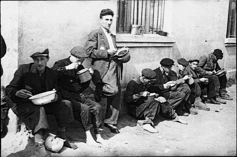 Henryk Ross photo of a Lodz Ghetto men alongside building eating from pails, c. 1940-1944. (Courtesy, Museum of Fine Arts, Boston)