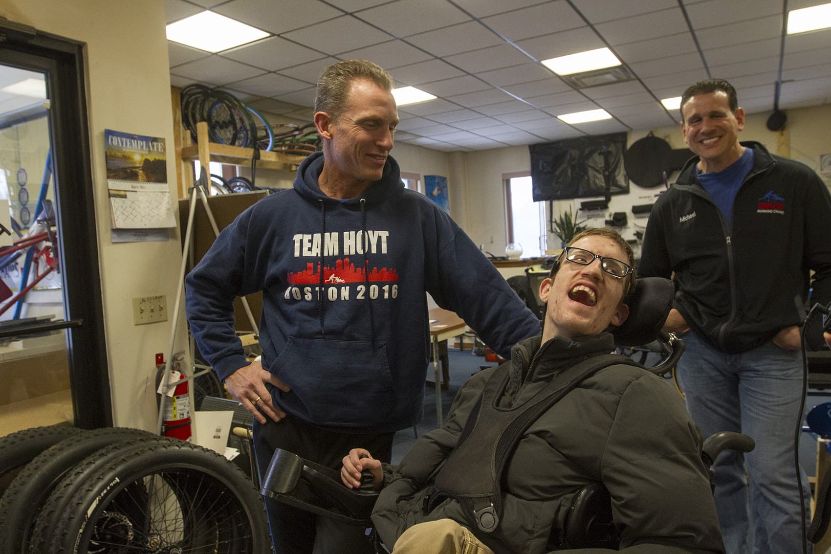 Ted Painter, left, and Nick Draper, will be competing in the 2017 Boston Marathon, using a chair built at Southbridge Tool and Manufacturing. Mike DiDonato, right, helped steer his family’s business into making Team Hoyt Running Chairs. (Joe Difazio for WBUR)