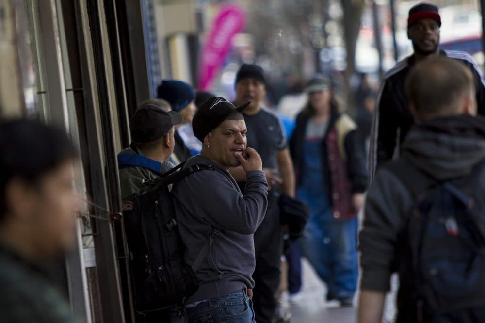 People -- including many immigrants -- bustle along Broadway in front of Full Service Laundry in Chelsea. (Jesse Costa/WBUR)