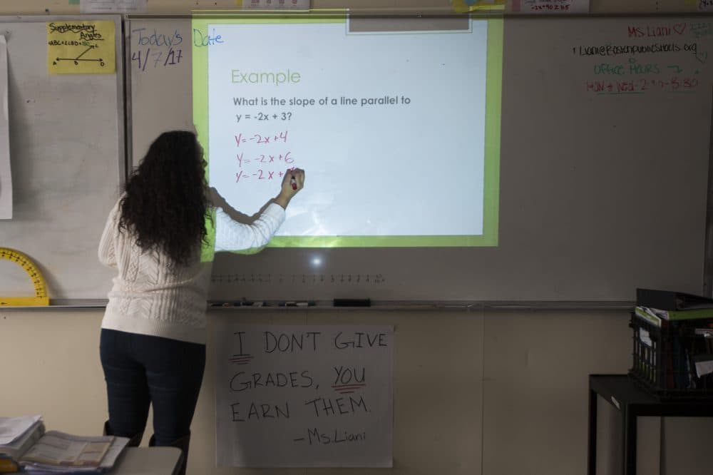 Teacher Roma Liani writes example equations on the whiteboard. (Jesse Costa/WBUR)