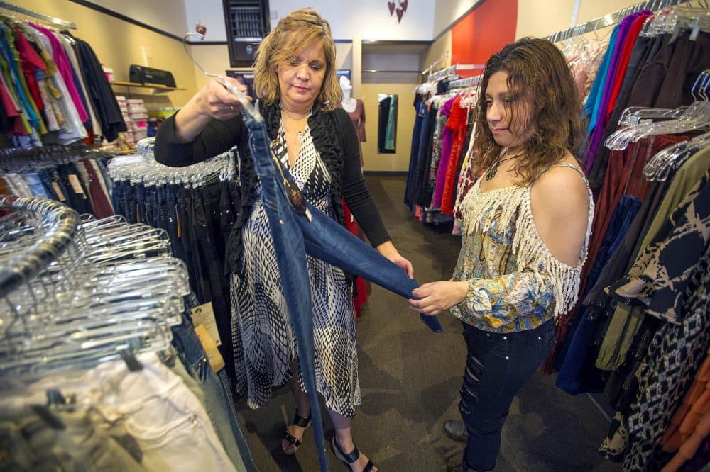 Fatima Ortiz, left, shows Gloria Rivas a pair of jeans at her clothing shop, Amazonia, on Broadway in Chelsea. (Jesse Costa/WBUR)