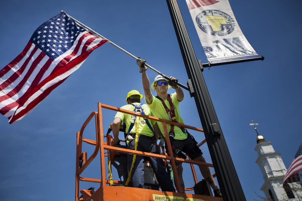 Southwick DPW worker Kris Anderson places American flags on lamp posts along College Highway in the downtown area of Southwick. (Jesse Costa/WBUR)