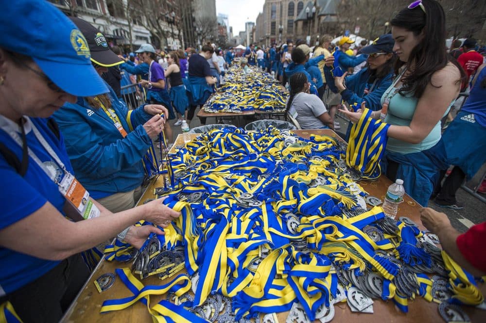 Marathon volunteers grab medals from the thousands that are piled up on tables stretching down Boylston Street. (Jesse Costa/WBUR)