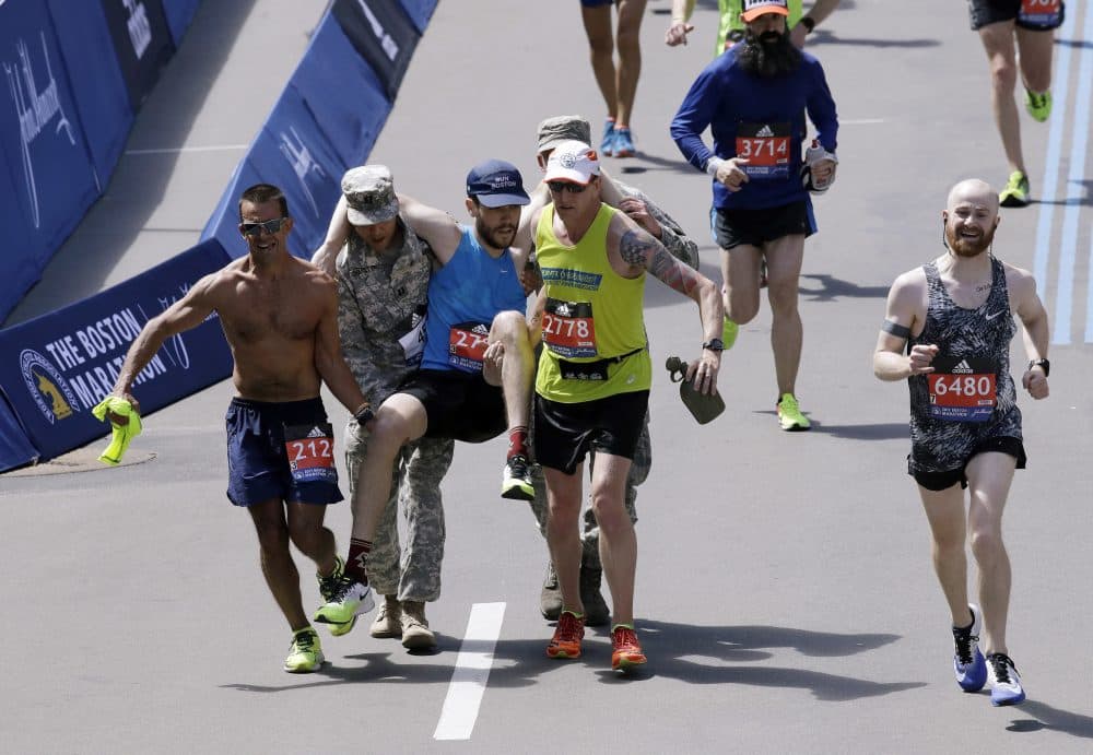 Jake Mogan, of San Francisco, is carried to the finish line by Franklin Tenorio, of Equador, left, and Bryan Stansberry, of Columbus, Ohio, and members of the military. (Charles Krupa/AP)