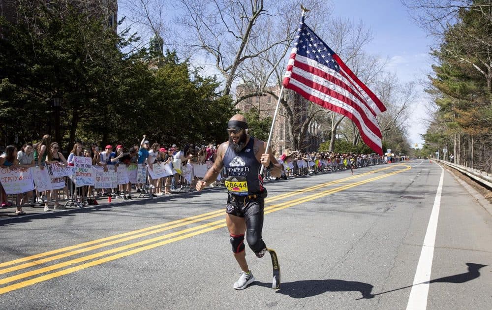 A runner with the words &quot;Semper Fi&quot; on his shirt and &quot;Operation Enduring Freedom&quot; on his flag runs through the Wellesley &quot;Scream Tunnel.&quot; (Robin Lubbock/WBUR)