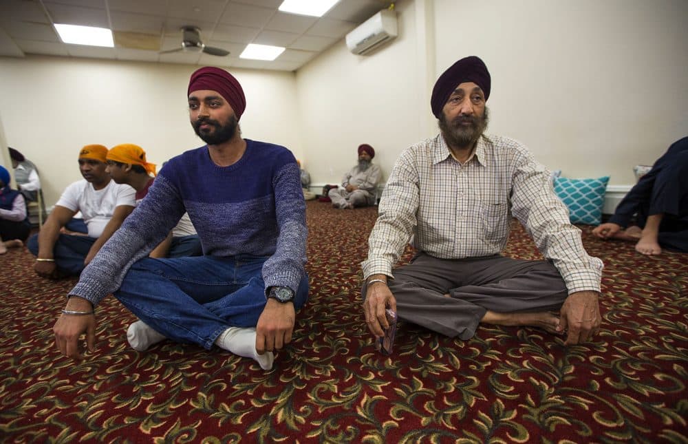 Kanwar Singh, left, and his father Jasbir sit on the floor together during the ceremony at the Sikh temple in Everett. (Jesse Costa/WBUR)