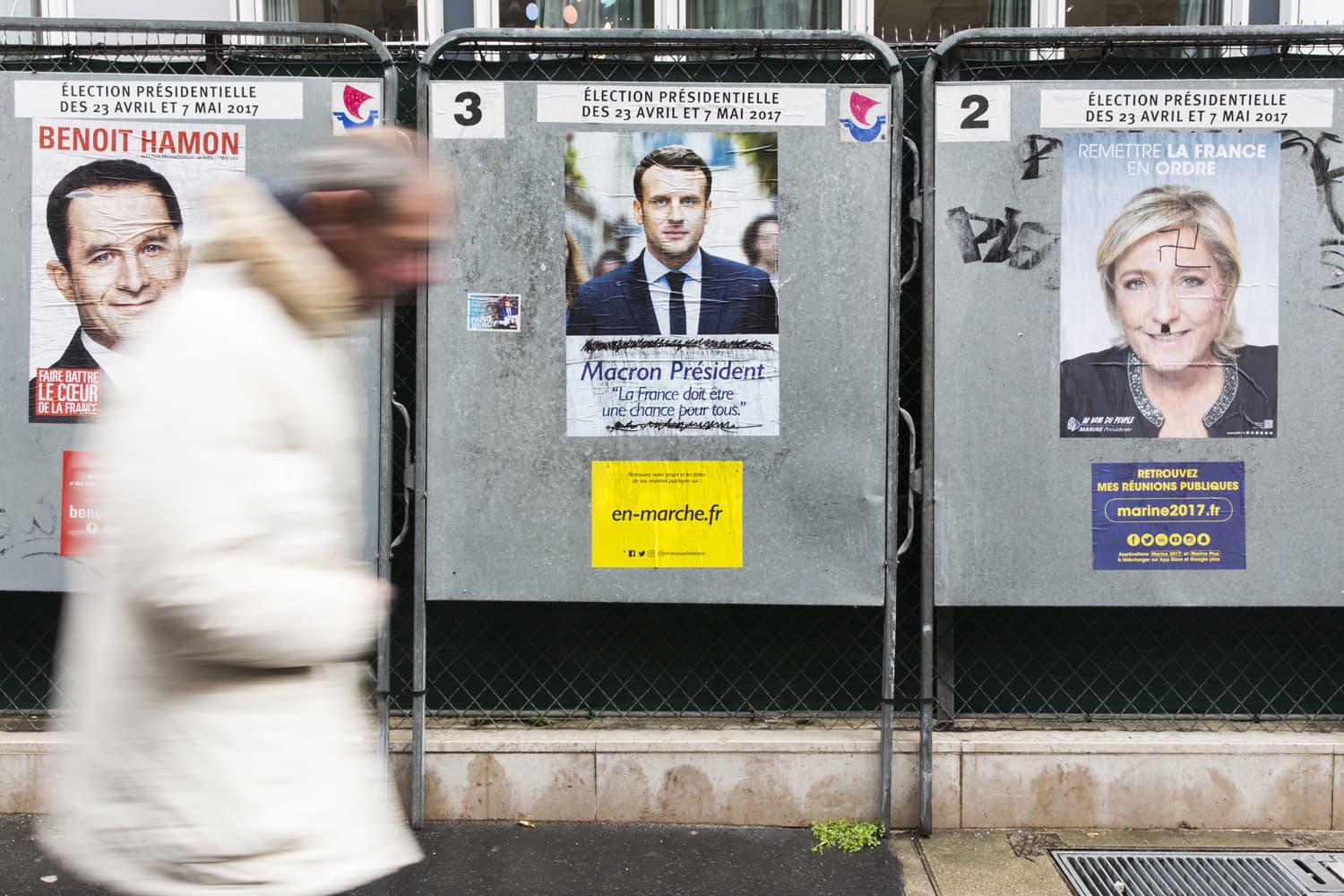 A man walks past electoral posters displaying the presidential candidates, Benoit Hamon, left, Emmanuel Macron, center, and Marine Le Pen in Paris, France. (Kamil Zihnioglu/AP)