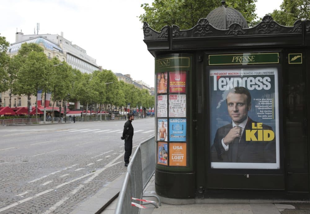 A police officer stands guard next to a newsstand displaying the cover of a news magazine depicting French president-elect Emmanuel Macron during a ceremony to mark the end of World War II on the Champs Elyses avenue in Paris, France, Monday, May 8, 2017. Macron defeated far-right leader Marine Le Pen handily in Sunday's presidential vote, and now must pull together a majority for his year-old political movement by mid-June legislative elections. (Michel Euler/AP)
