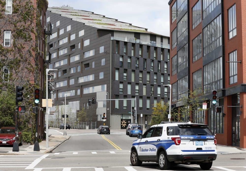 A Boston police vehicle patrols Monday near the scene of a double murder in the penthouse of the Macallen Building, center, in Boston. Bampumim Teixeira is charged with killing Dr. Lina Bolanos and Dr. Richard Field on Friday night. (Michael Dwyer/AP)