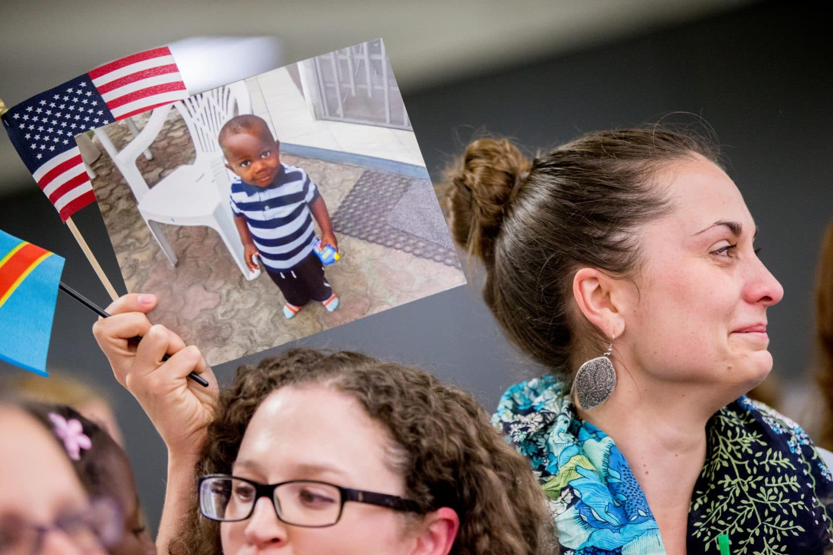 If inter-country adoptees deserve to feel secure in the nation they call home, writes Margaret Homans, so do all the other immigrants who are part of our national family. Pictured: Sarah from Philadelphia holds up a photograph of Gedeon, 3, as a group of families waiting for long-stalled exit permits for adopted children from the Congo gathered for a welcome celebration at Dulles International Airport on Wednesday, Nov. 11, 2015. (Andrew Harnik/AP)