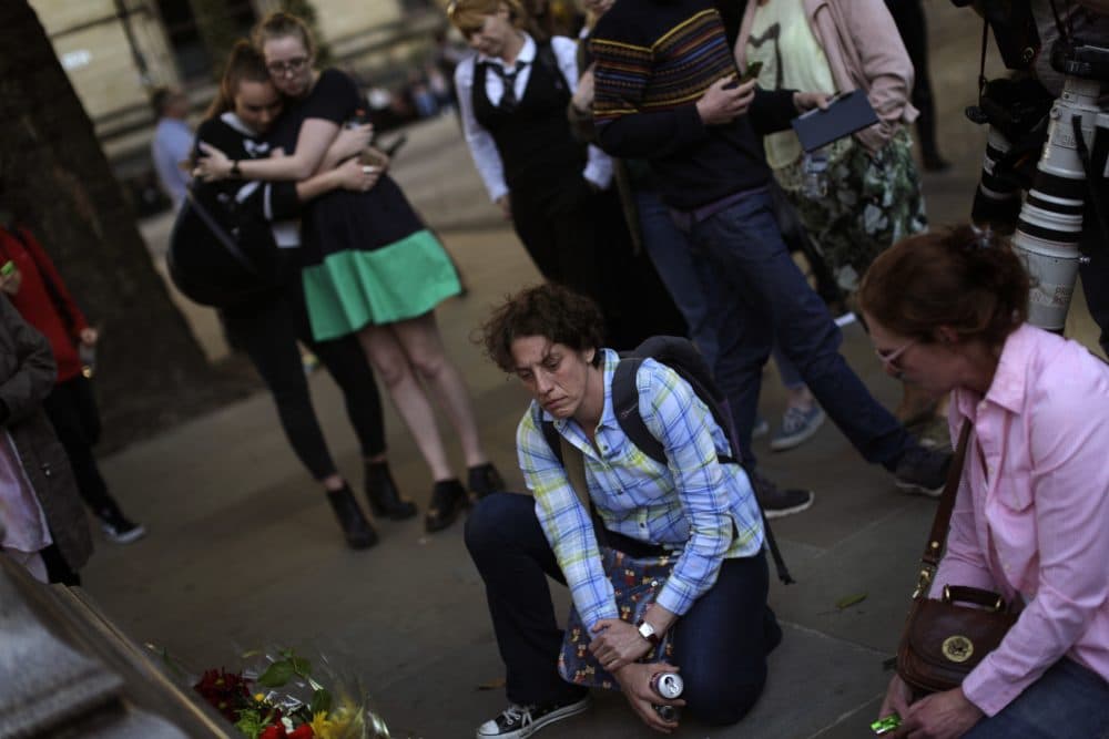 After two days of studying the faces of the individuals killed in the Manchester bombing, writes Julie Wittes Schlack, I feel compelled to also peer into the face of the man who blew himself to bits. Pictured: People stand next to flowers after a vigil in Albert Square, Manchester, England, Tuesday May 23, 2017, the day after the suicide attack at an Ariana Grande concert that left 22 people dead. (Emilio Morenatti/AP)