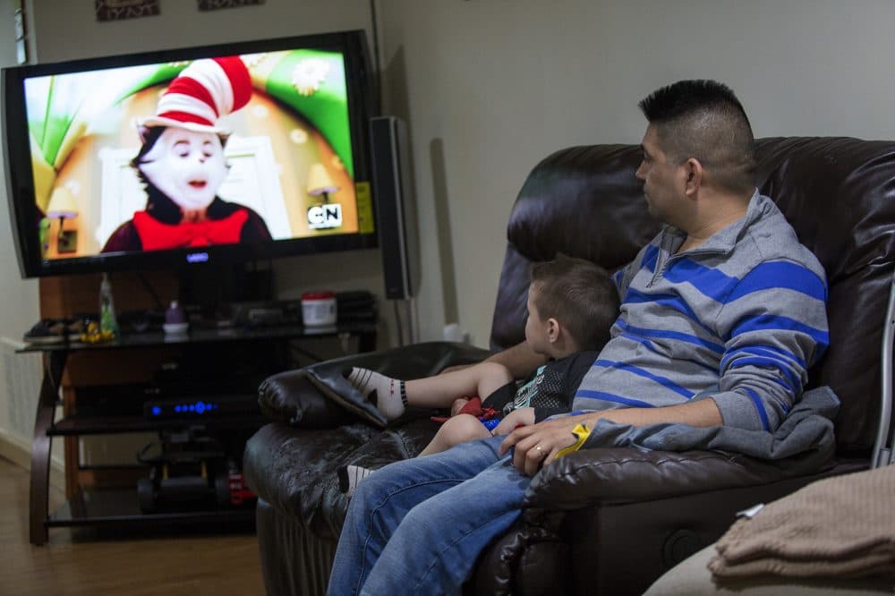 Jose Flores watches television with his young son in 2017. (Jesse Costa/WBUR)