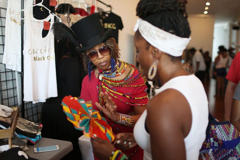 Shalair Armstrong, owner of the retail store Diaspora Africa, speaks to a customer at the Black Market in Dudley Square. (Hadley Green for WBUR)