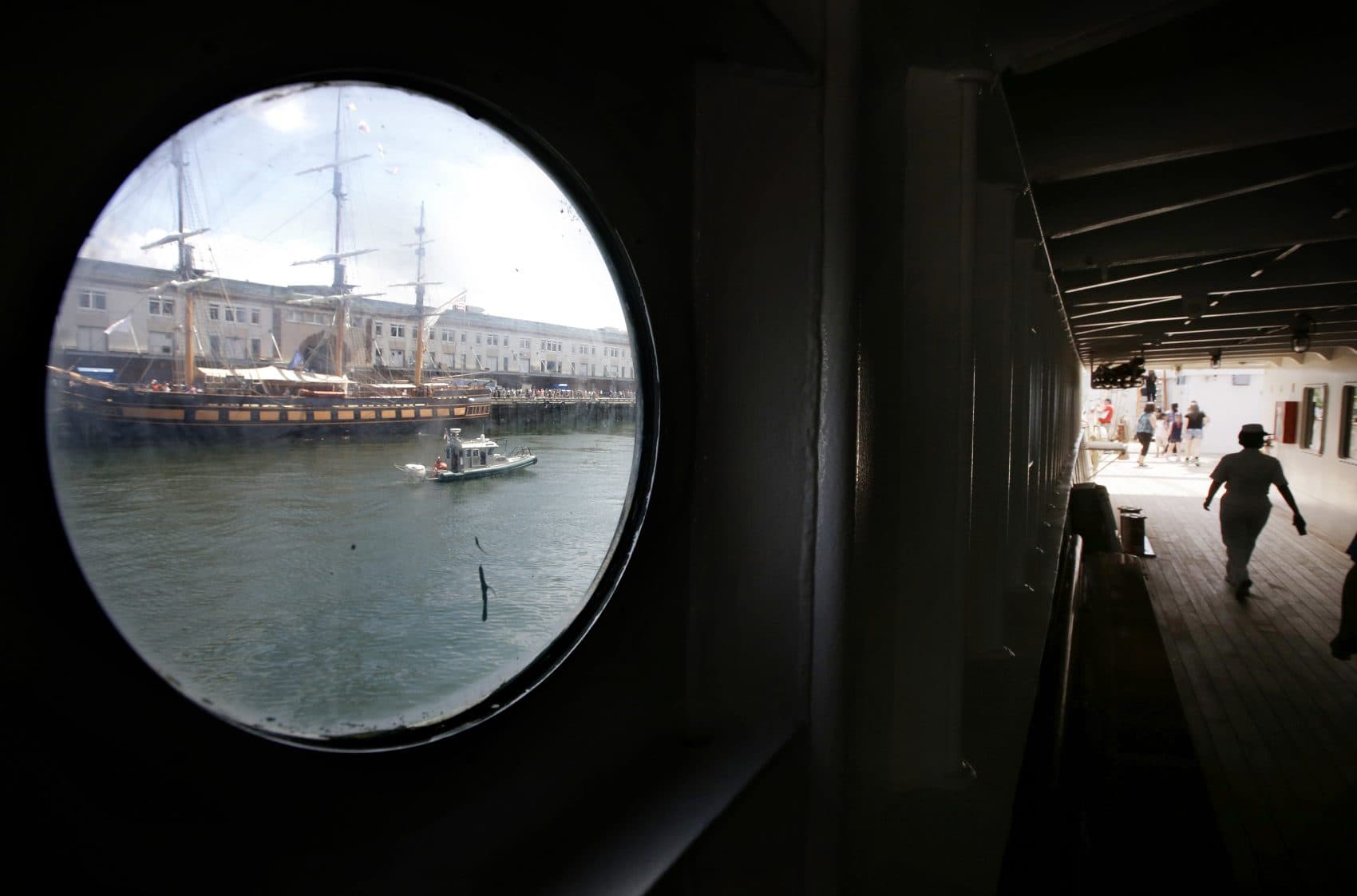 The tall ship Oliver Hazard Perry, top left, is viewed through a porthole on the Peruvian Navy tall ship Union as passers-by, right, walk along a deck aboard the Union on Sunday in Boston. (Steven Senne/AP)
