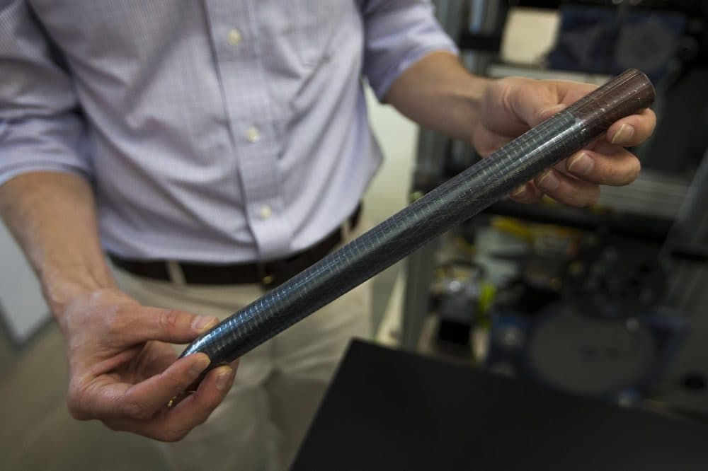 Sasha Stolyarov holds a preform, which is the starting material where devices are integrated. Functionality is created at this level by introducing semiconducors and metals to the preform which is then drawn or pulled into fibers. (Jesse Costa/WBUR)
