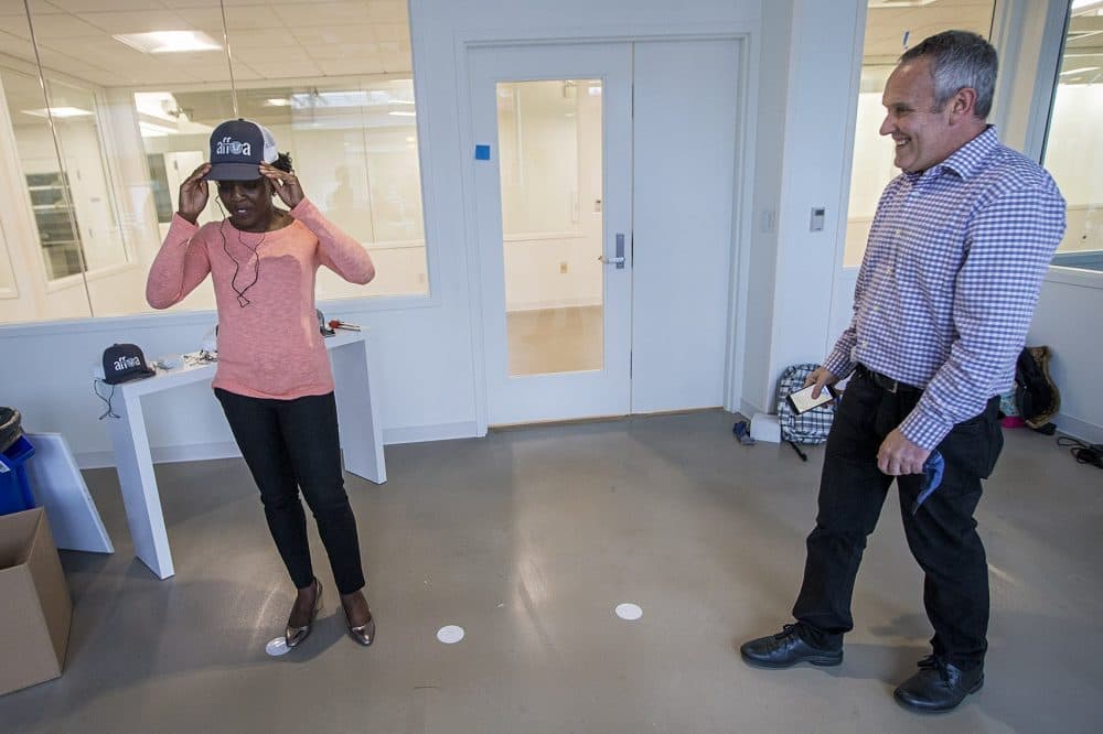 WBUR reporter Zeninjor Enwemeka tries on an AFFOA trucker hat which serves as an optical receiver working with LED lights installed above it. The hat has an audio plug to attach earbuds to listen to the sound that the lights are streaming. (Jesse Costa/WBUR)