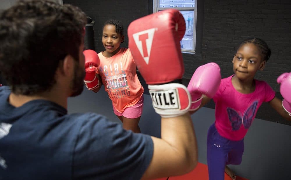 Vekaila and Vehari Brade, 8, take aim at Fredy Melo's gloves. (Robin Lubbock/WBUR)