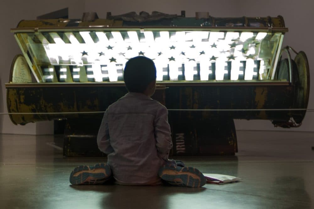 Nine-year-old Danny Zheng colors on the floor in front of Nari Ward's &quot;Tanning Bed.&quot; (Jesse Costa/WBUR)