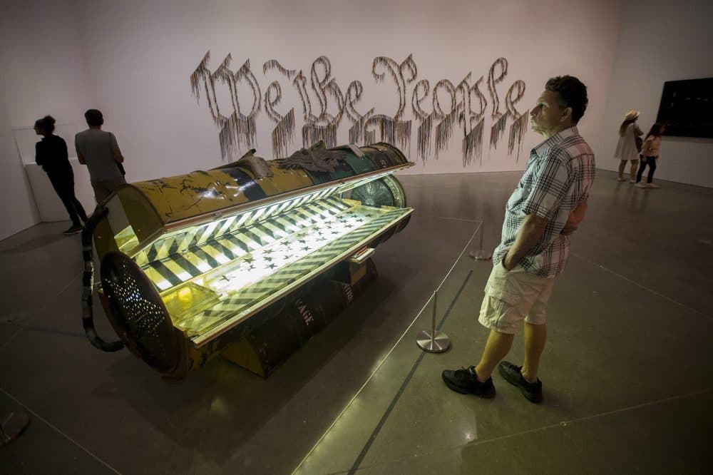 A museum patron looks at Nari Ward's &quot;Tanning Bed.&quot; The work, &quot;We The People,&quot; is seen in the background. (Jesse Costa/WBUR)