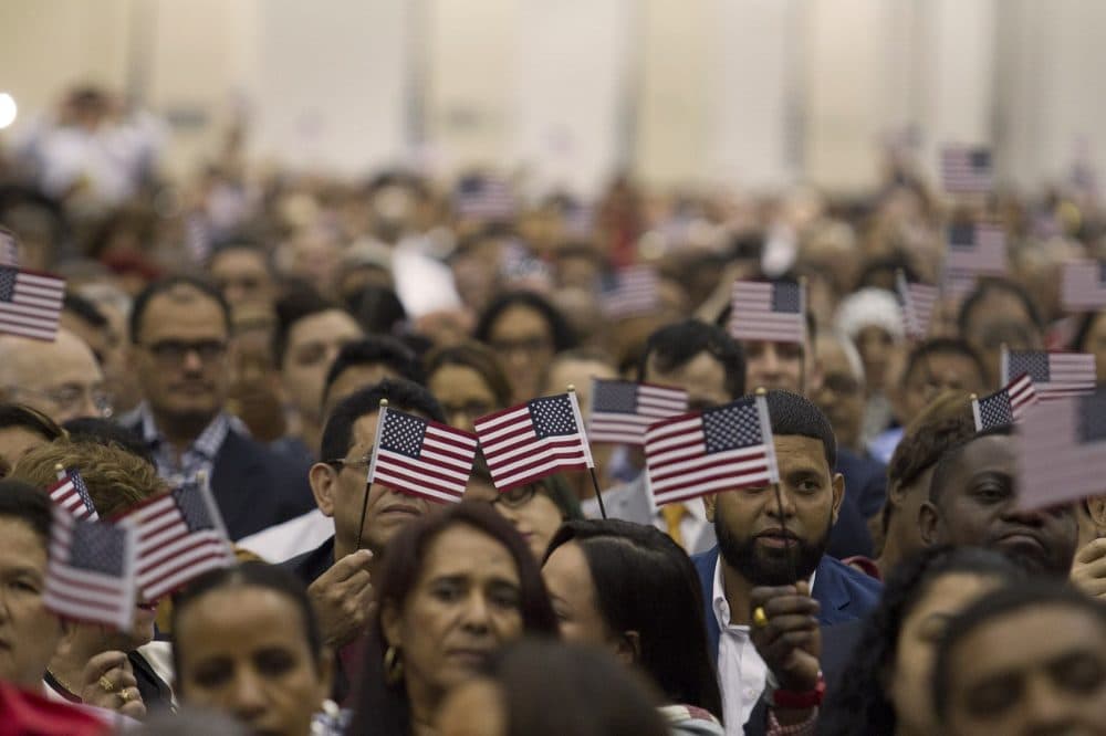 Brand new U.S. citizens waving flags during a rendition of 'America the Beautiful' at the Hynes Convention Center in Boston, June 2016. (Joe Difazio for WBUR)