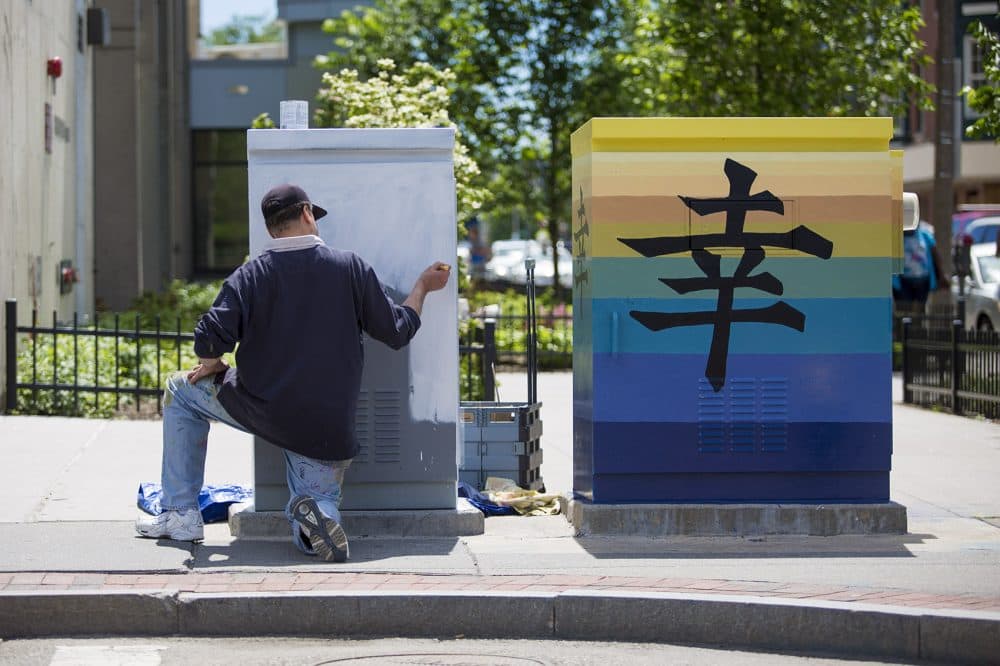 Jeffrey Powers whitewashes an electrical box next to one he has already painted on Mass. Ave. (Jesse Costa/WBUR)