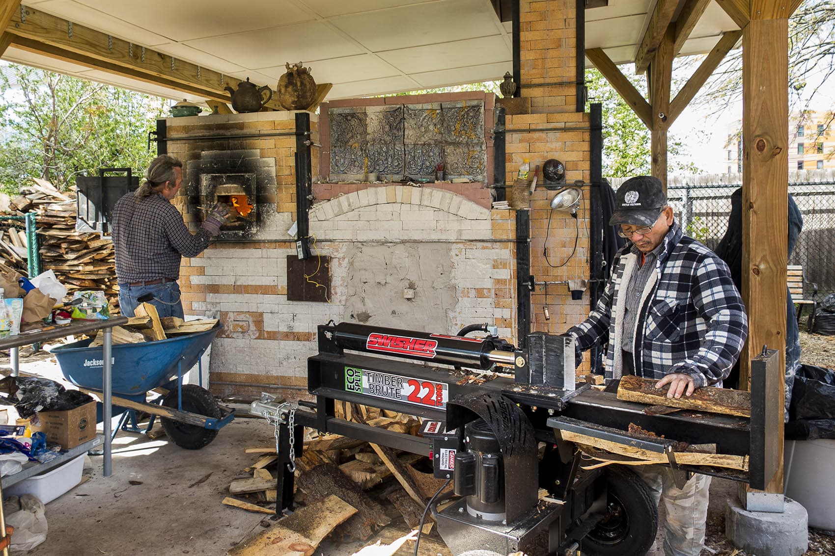 Yary Livan works at his kiln. His student John Kondra loads wood into the stone fireplace. (Andrea Shea/WBUR)