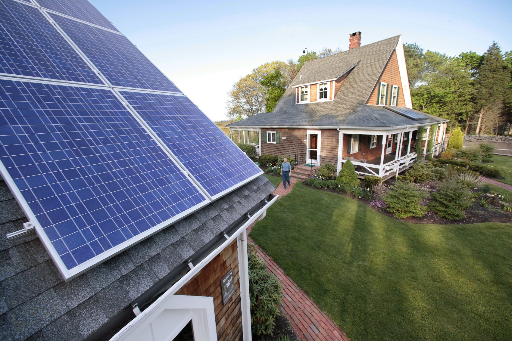 In this 2009 file photo, a man walks from his house to his garage where solar energy panels are mounted on the roof in Marshfield, Mass. (Stephan Savoia/AP)