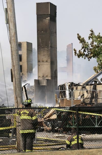 Firefighters pause near the destroyed remains of an under-construction apartment complex Sunday in Waltham. (Steven Senne/AP)