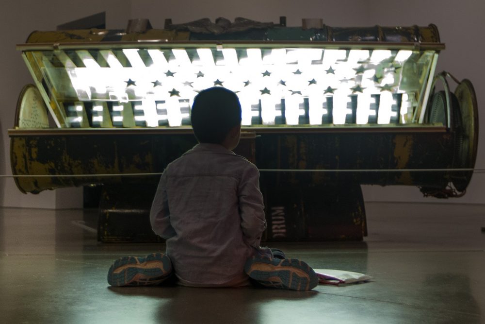 A 9-year-old boy colors on the floor in front of Nari Ward's &quot;Tanning Bed&quot; at the ICA. (Jesse Costa/WBUR)