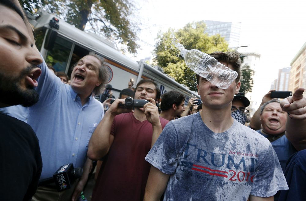 A man wearing a T-shirt bearing the name of President Donald Trump, right, is hit by a flying plastic bottle of water near the rally. (Michael Dwyer/AP)