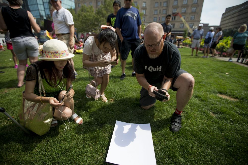 Bruce Myren, of Cambridge, uses a camera lens to project the eclipse onto a sheet of paper for viewing. (Jesse Costa/WBUR)