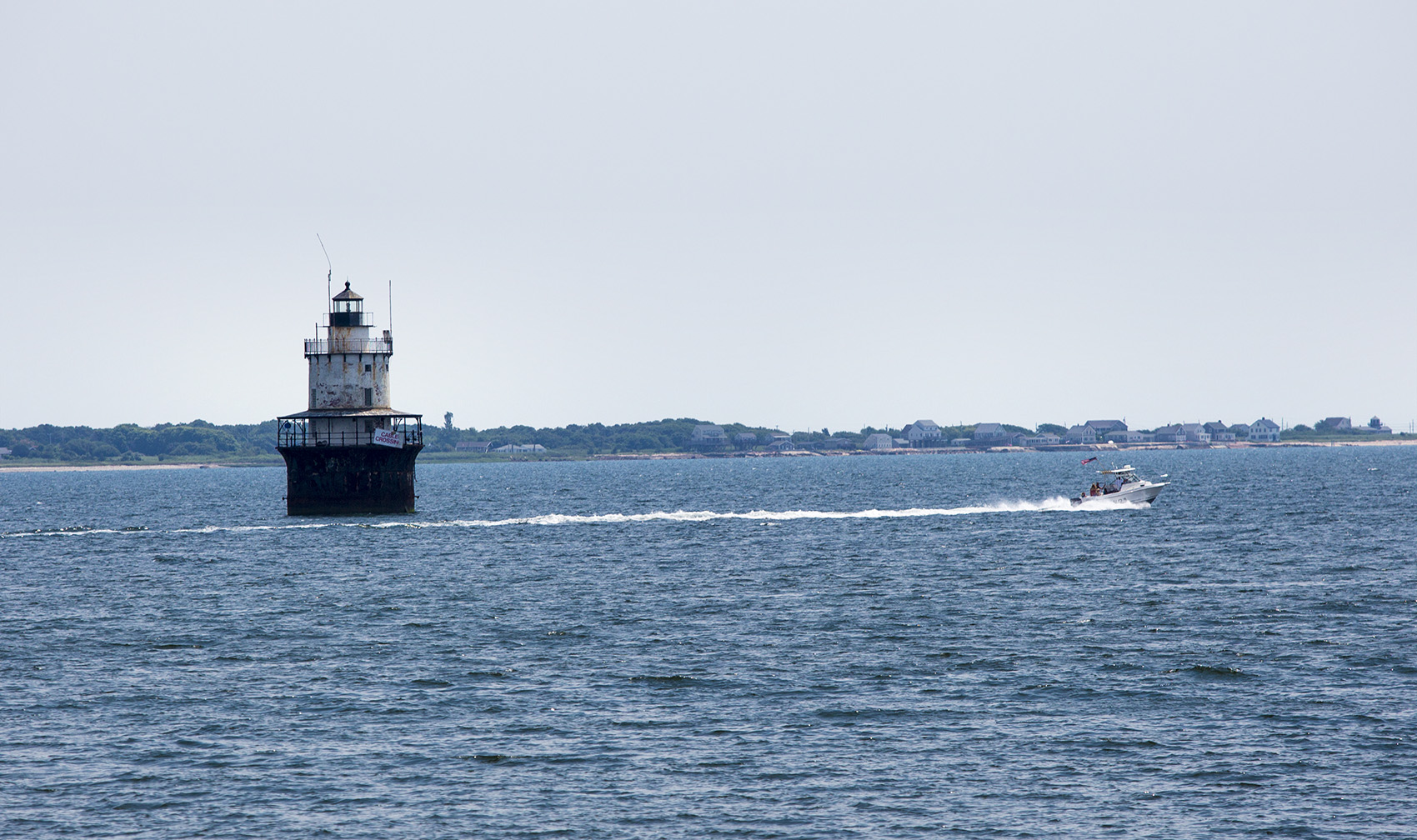A boat speeds by the Butler Flats Lighthouse at the mouth of the Acushnet River at Buzzards Bay. (Jesse Costa/WBUR)