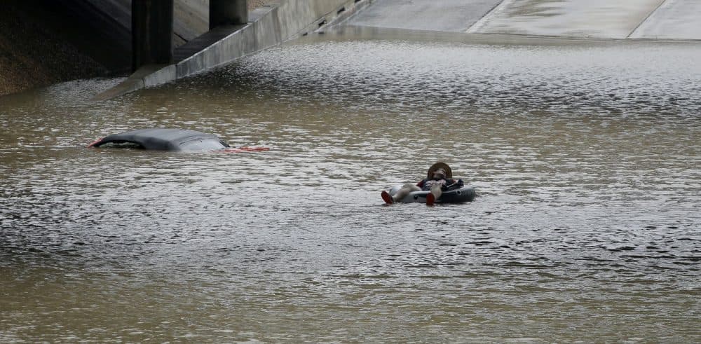 A man floats past a stalled car submerged on a flooded freeway. (Charlie Riedel/AP)